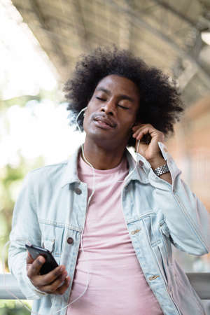 Portrait of afro american man with casual clothes and afro hairstyle enjoying music from his smart phone. Funny and relaxing moments.の写真素材