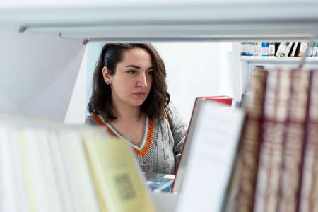 Young Caucasian woman looking at books in a library. Selective focus. Space for text.