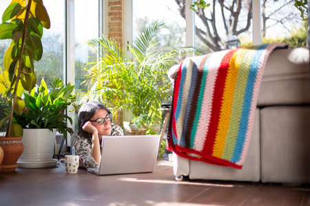 Adult woman lying on the floor of her house. She is using a laptop computer. Work at home.の写真素材