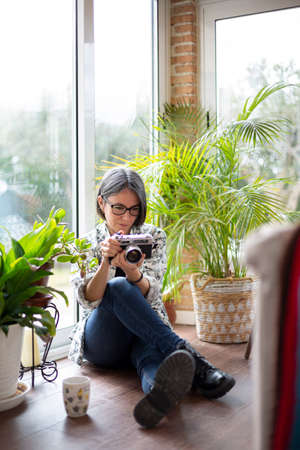 Adult woman at home using an analog photo camera. Space for text.の写真素材