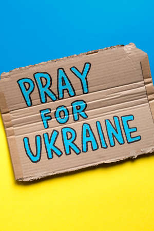 Hand drawn poster with slogan Pray For Ukraine on Ukrainian flag.