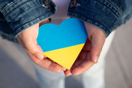 Close up of a small child's hands holding a heart in the colors of the Ukrainian flag showing support and solidarity. Protest against Russian invasion.の写真素材