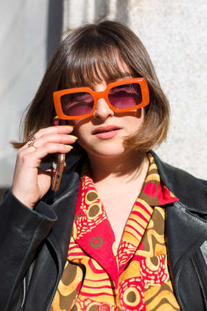 Outdoor portrait of young caucasian woman with sunglasses talking on the phone. Fashion and lifestyle concept. Close up.の写真素材