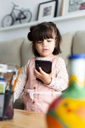 Little Latin American girl watching with attention something on a smart phone at home. Concept of minors and use of technology.の写真素材