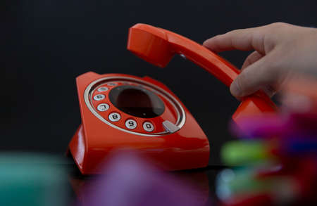Close up of a person's hand hanging or picking up a modern desktop telephone. Selective focus.