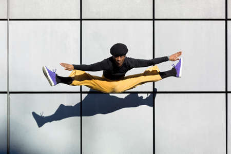 Young adult African American man jumping on a wall. Dancer doing acrobatics in the air. Original look, 90's aesthetics. Urban lifestyle. Space for text.の写真素材
