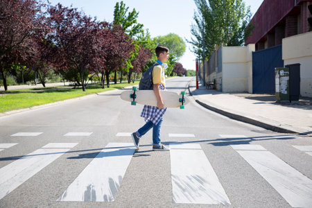 High school student boy with longboard skate crossing street. Space for text.の写真素材
