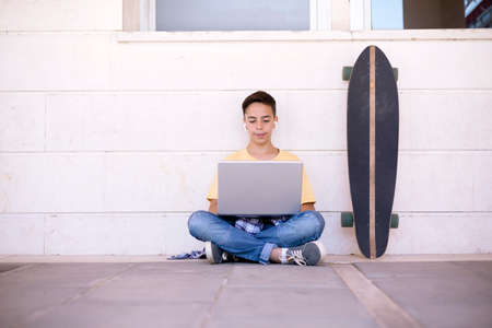 Caucasian teenage boy sitting on the floor using a laptop computer. Space for text.の写真素材