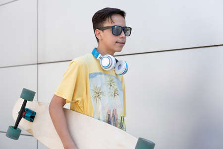 Closeup of caucasian teenage boy with skateboard. He is isolated on a wall. Vacation and urban...