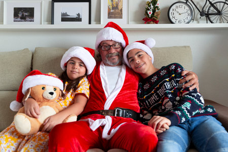 Christmas at home. Family portrait of grandfather dressed as Santa Claus hugging his grandchildren.の写真素材