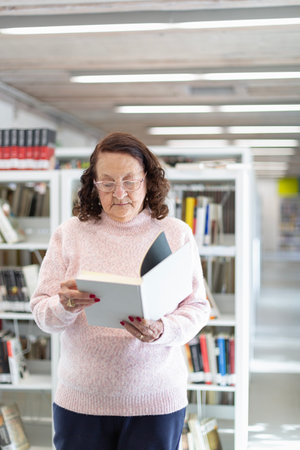 Caucasian older woman reading a book in a public library. Entertainment concept of elderly people.の写真素材