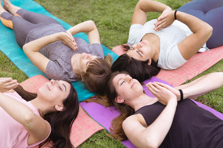 Group of caucasian female friends practicing yoga outdoors. They are lying on the grass in relaxing posture.の写真素材