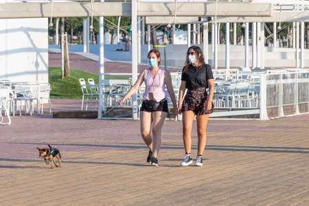 Huelva, Spain - May 23, 2020: Woman walking her dog by Huelva promenade at sunset, wearing protective or medical face mask during the alarm state and quarantine in Spain.のeditorial素材