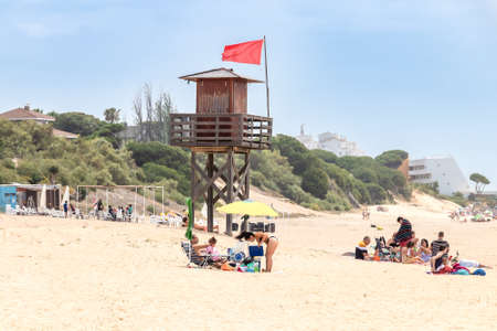 Punta Umbria, Huelva, Spain - May 30, 2020: People are in the beach with red flag on lifeguard tower in El Portil Beach.のeditorial素材