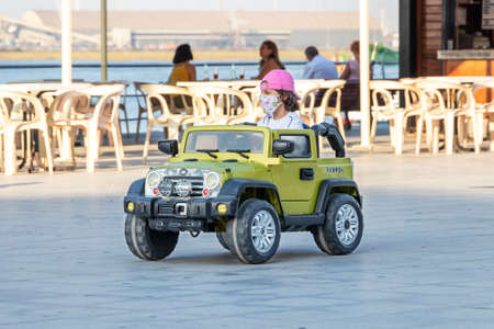 Punta Umbria, Huelva, Spain - July 10, 2020: A kid playing with electric car is wearing protective mask due to covid-19. New normal in Spainのeditorial素材