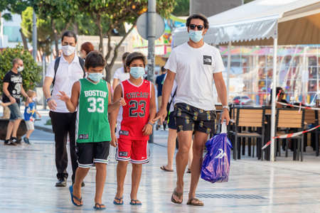 Punta Umbria, Huelva, Spain - July 10, 2020: Father with two children  walking by street wearing protective mask due to covid-19. New normal in Spainのeditorial素材