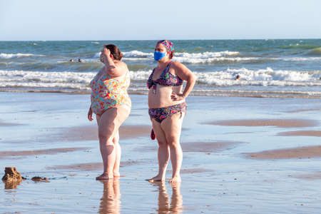 Punta Umbria, Huelva, Spain - August 2, 2020: two overweight women at the beach wearing protective or medical face masks. New normal in Spain with social distancingのeditorial素材
