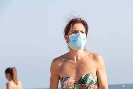 Punta Umbria, Huelva, Spain - August 7, 2020: Woman walking by the beach wearing protective or medical face masks. New normal in Spain with social distancingのeditorial素材