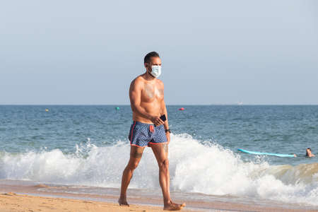 Punta Umbria, Huelva, Spain - August 7, 2020: Man walking by the beach wearing protective or medical face masks. New normal in Spain with social distancingのeditorial素材
