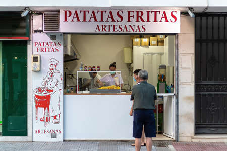 Punta Umbria, Huelva, Spain - August 7, 2020: Vendor in a local sells potato chips. Fried potato are typical local street food. She is wearing protective mask due to covid-19 coronavirusのeditorial素材