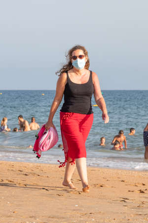 Punta Umbria, Huelva, Spain - August 7, 2020: Couple walking by the beach wearing protective or medical face masks. New normal in Spain with social distancingのeditorial素材