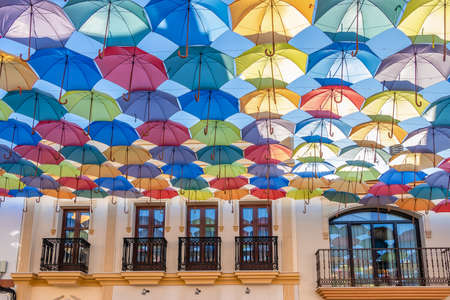 The sky is full of colorful umbrellas. Street with umbrellas in the sky in the village San Bartolome de la torre. Summer decoration and sun protection. Huelva province, Andalusia, Spainの写真素材