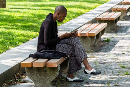 New York City, USA - June 10, 2017: African american woman using her mobile phone in a public park during coffee breakのeditorial素材