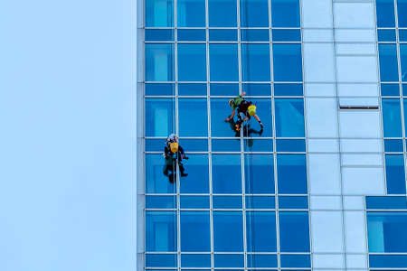 Window washers cleaning the glass facade of a modern building, high risk work