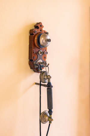 An old vintage corded telephone for communication hangs on a yellow wall. One of the first...