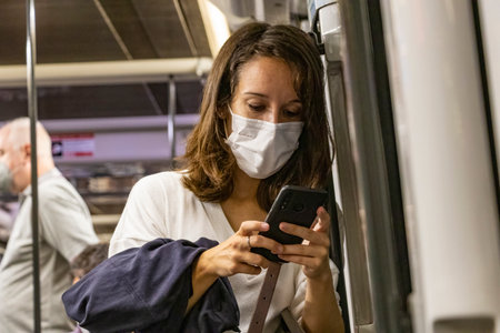 Barcelona, Spain - September 21, 2021: A woman is using her mobile phone while is traveling in the subway. She is using a protective face mask due to coronavirus covid-19 epidemicのeditorial素材