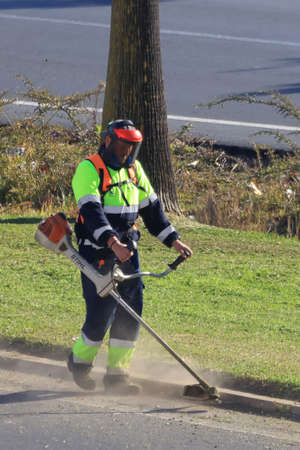 Huelva, Spain - January 12, 2021: workers mowing lawn with grass trimmer outdoors on sunny dayのeditorial素材