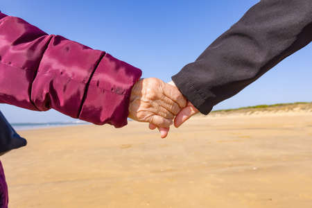 A mature woman holds her elderly mother's hand while walk by the beachの写真素材