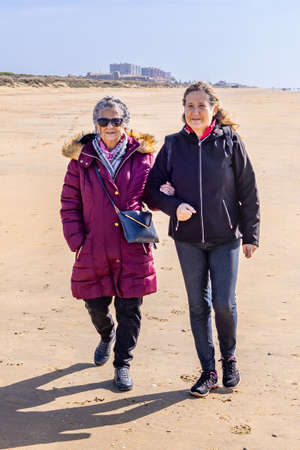 A mature woman walking with her elderly mother by the beach at autumnの写真素材