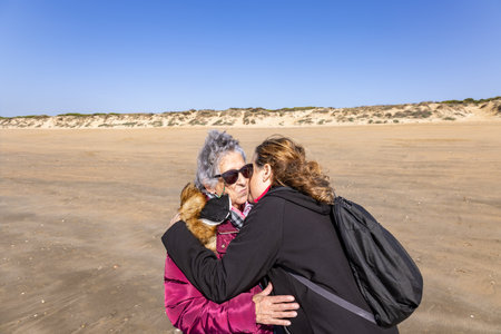 A mature woman kisses and hugs her elderly mother on the beachの写真素材