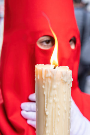 The candle in flame of a young Nazarene with a red hood doing his penance station in the Holy Week procession. Selective focus with candle flame only in focusの写真素材