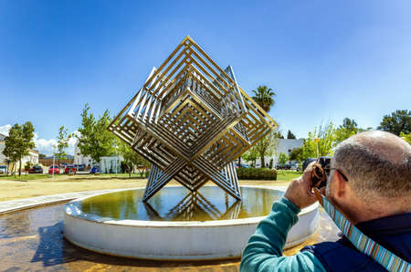 Huelva, Spain - April 28, 2022: A photographer doing a photo to the stainless steel cube monument in the gardens of the Campus of âEl Carmenâ of the Huelva University.のeditorial素材