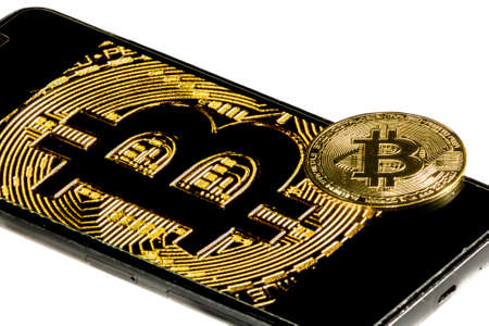 Close-up of gold Bitcoin coins with mobile phone in white background.の写真素材