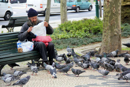Portugal, Lisbon. Circa 10th April 2014. Homeless man sharing his meal with birds Picture taken on the road Rua da Liberdade in Lisbon Portugal in April 2014のeditorial素材