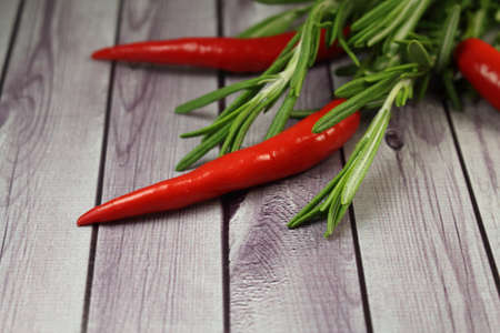Red hot peppers and sprigs of green rosemary. Closeup, side view. Lie on a background of simulated wood planks.の写真素材