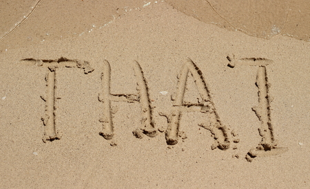 Writing inscription Thai on a wet sand in a sunny day. Sea water approaches the inscriptionの写真素材
