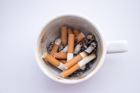 Pile cigarette butts with ashes in a dirty white cup instead of ashtray isolated on a white background.の写真素材