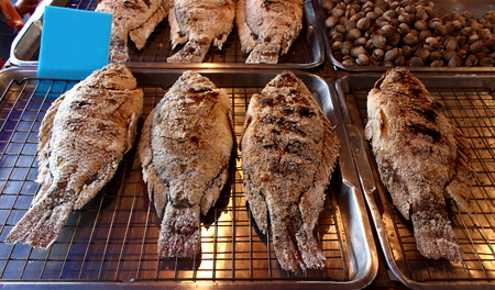 Fried fish in salt on grill on the counter of a market trader. Traditional Asian street food