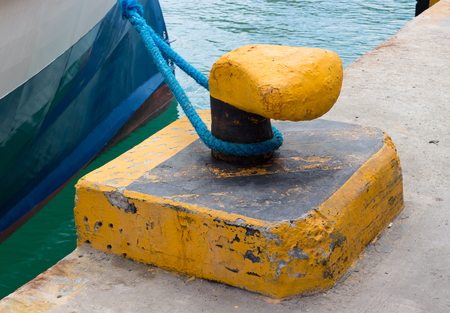 Bitt is tied around a thick blue sea rope. Mooring bollard on the wharf with hawser of ship....