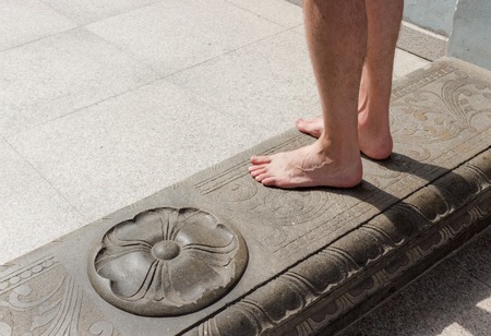 The bare feet of a male traveler on the doorstep of a Sri Maha Mariamman Temple adorned with an ancient ornament at Kuala Lumpur, Malaysiaの写真素材