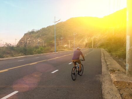 Unrecognizable man in the sun rays rides a bicycle on a mountain road to the sunset