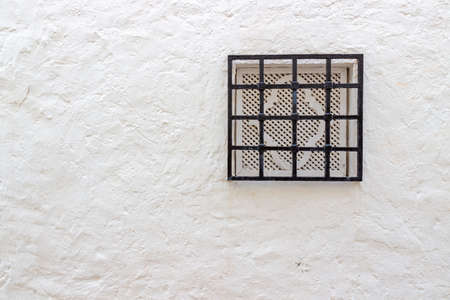 Closed small window with iron grate in white stone wall. Traditional house in the medina of Hammamet town, Tunis. House details in North Africaの写真素材