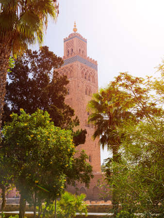 Sunny view on Minaret of Kutubiyya Mosque against the background bright green foliage of tropical trees in Marrakesh, Morocco. Holiday travel postcardの写真素材
