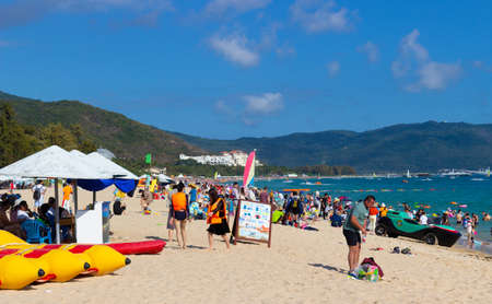 China, Hainan island, Sanya - January 23, 2020: Chinese tourists relax on the sandy beach of a tropical island of a popular resort:のeditorial素材