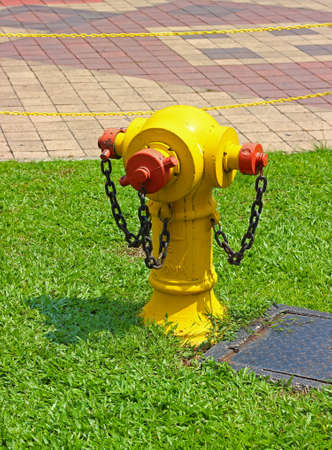 Typical old yellow fire hydrant with rusty chains on the lawn in Kuala Lumpur city on a sunny dayの写真素材