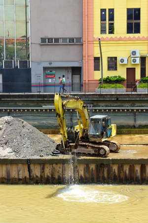 Kuala Lumpur, Malaysia - Mart 12, 2019: yellow excavator that cleans the bed of the Klang and Gombak Rivers from garbage in the project River of Life in the center of Kuala Lumpurのeditorial素材